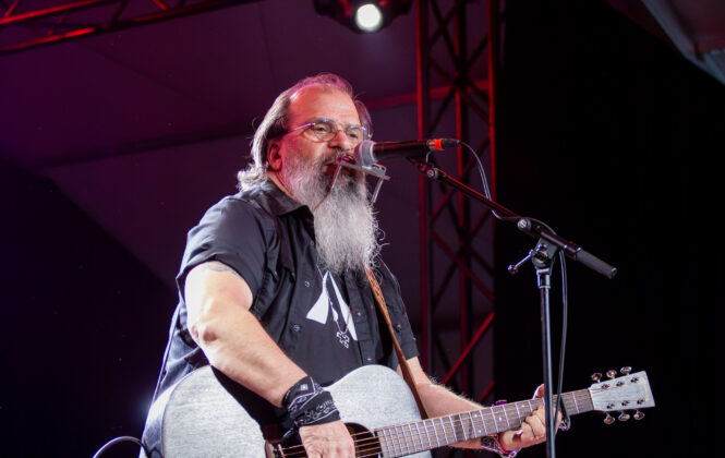 Man looks at crowd while singing with guitar on stage.