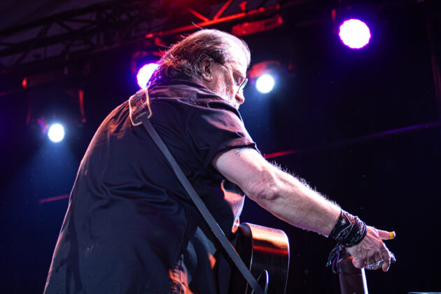 Man pulls out harmonica onstage while holding guitar