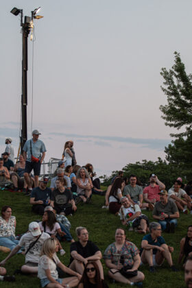 Crowds of people sit on grassy hill looking ahead