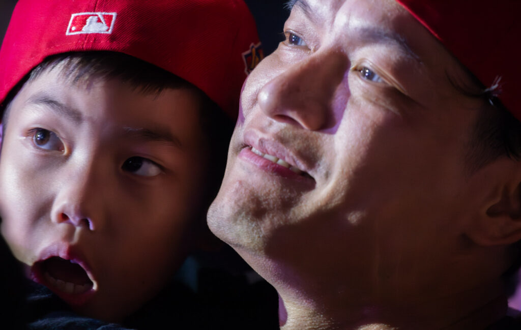Young boy and dad watch performance wearing backwards red baseball hats