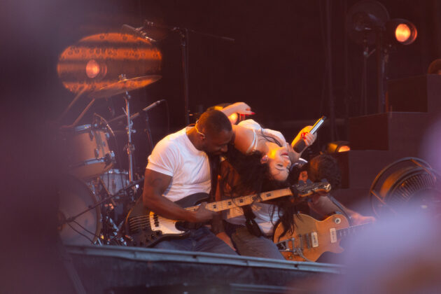 Woman in white dress leans on her band on stage