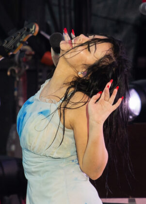 Woman raising her hands and leaning back in white dress on stage
