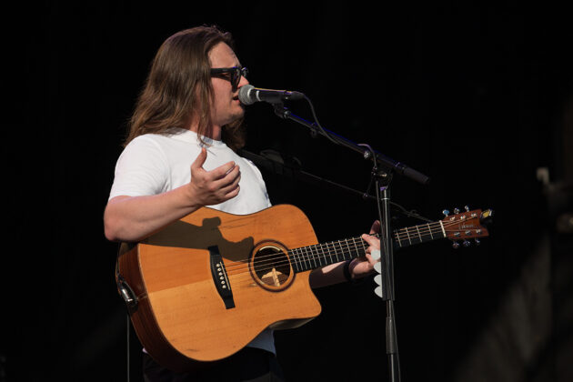Man holding guitar chats into mic on stage
