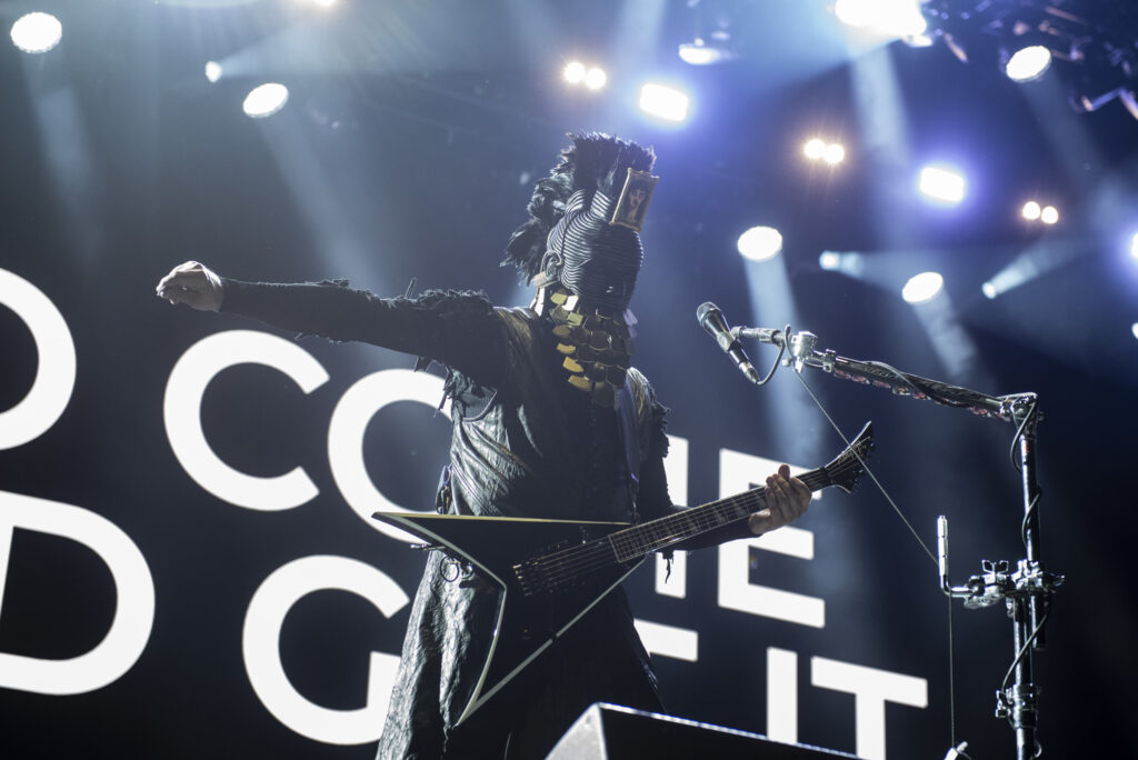 Man wearing Day of the Dead inspired clothes and mask holds electric guitar on stage