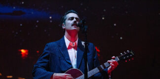 Bluesfest Day 6 review: Lord Huron, Lucy Dacus invite nostalgia with atmospheric indie rock Man looks up while singing into mic and playing guitar on stage