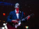 Bluesfest Day 6 review: Lord Huron, Lucy Dacus invite nostalgia with atmospheric indie rock Man looks up while singing into mic and playing guitar on stage